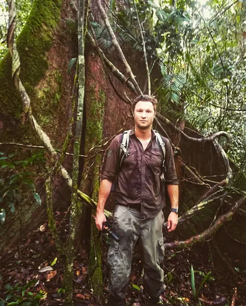 Tim standing beneath a giant rainforest tree in Borneo