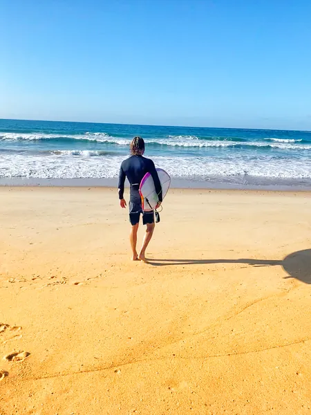 Tim walking down to the water with a surfboard